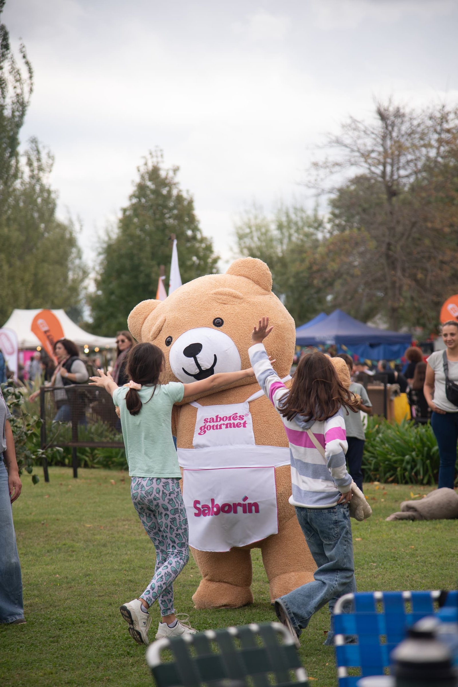 Chicas abrazando a Saborín, el oso mascota de Sabores Gourmet