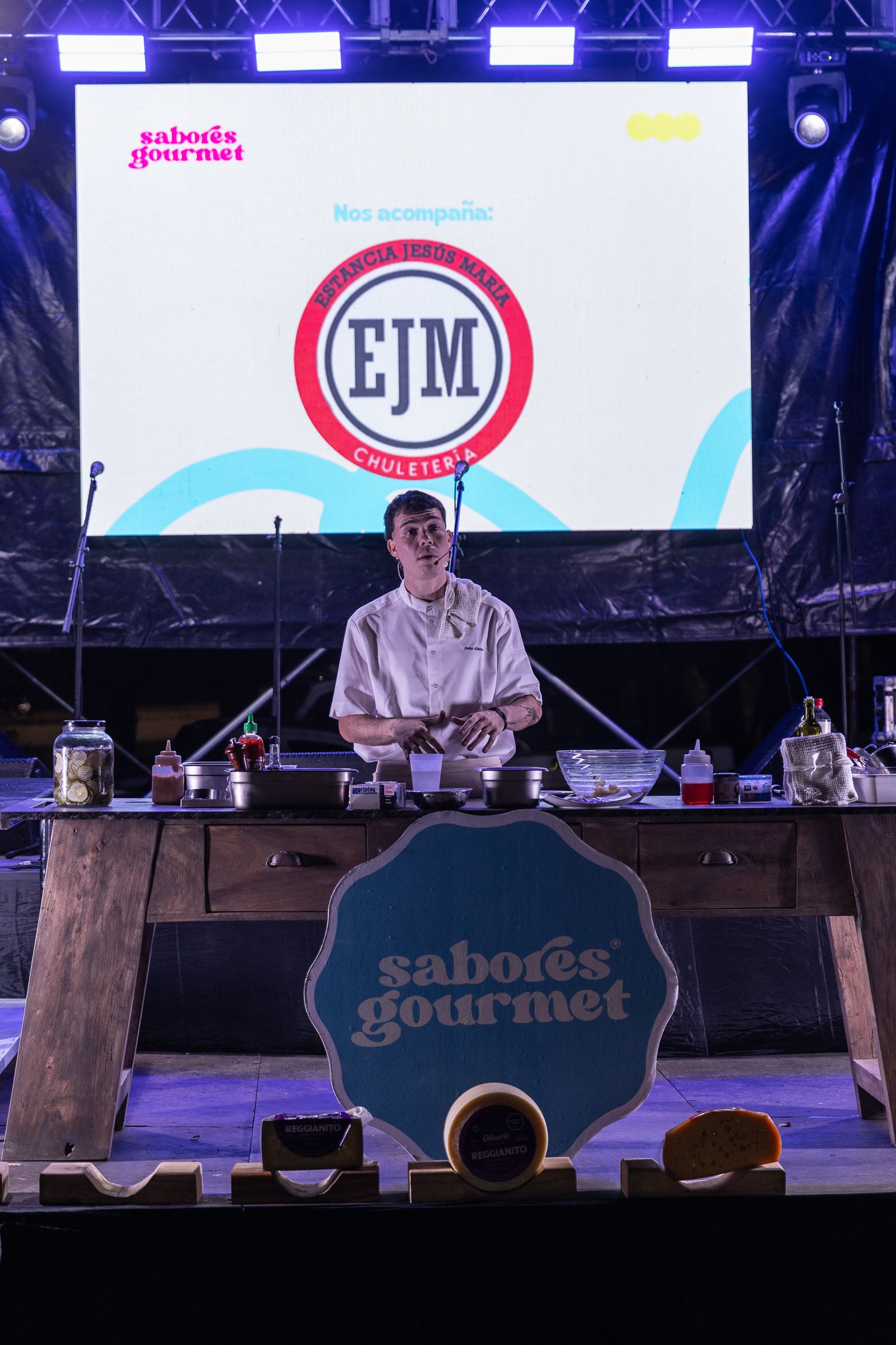 Chef preparando un asado nocturno frente al escenario iluminado de púrpura