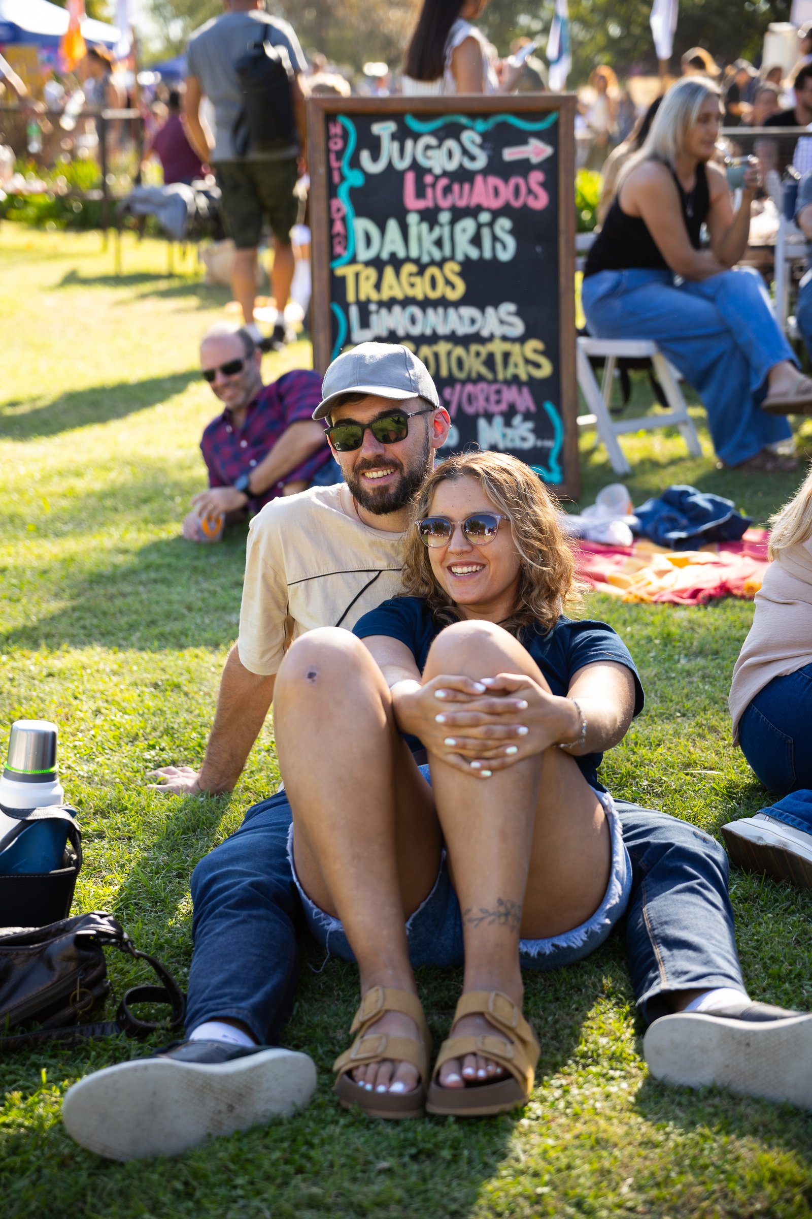 Pareja sentada en el pasto junto a un cartel de jugos y licuados
