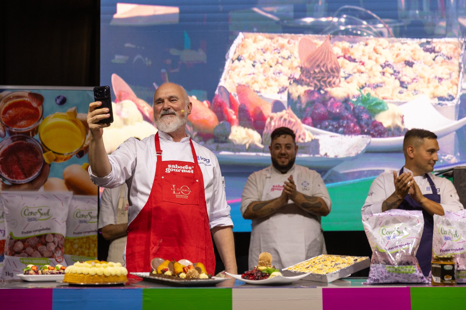 Chef Osvaldo Gross cocinando sobre el escenario junto a la pantalla con su nombre